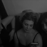 Girls on couch one looking at her phone.