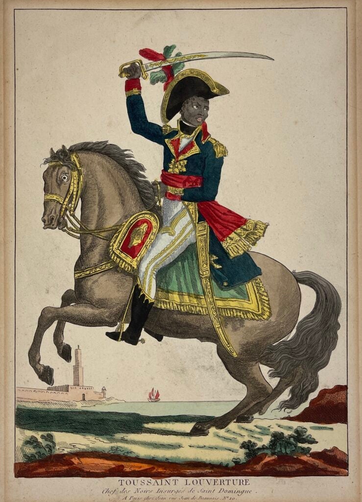 The image depicts Toussaint L’Ouverture, a formerly enslaved black man, in regal clothing of yellow, red, and green. He rides horseback on a decorated saddle and holds a sword raised above his head, which is covered by a captain's hat. L’Ouverture's fierce expression rests on an intense face, indicating the mysticism surrounding his appearance. L’Ouverture is placed in the foreground, dominating the frame, while a boat sails away into the Caribbean Sea behind him.